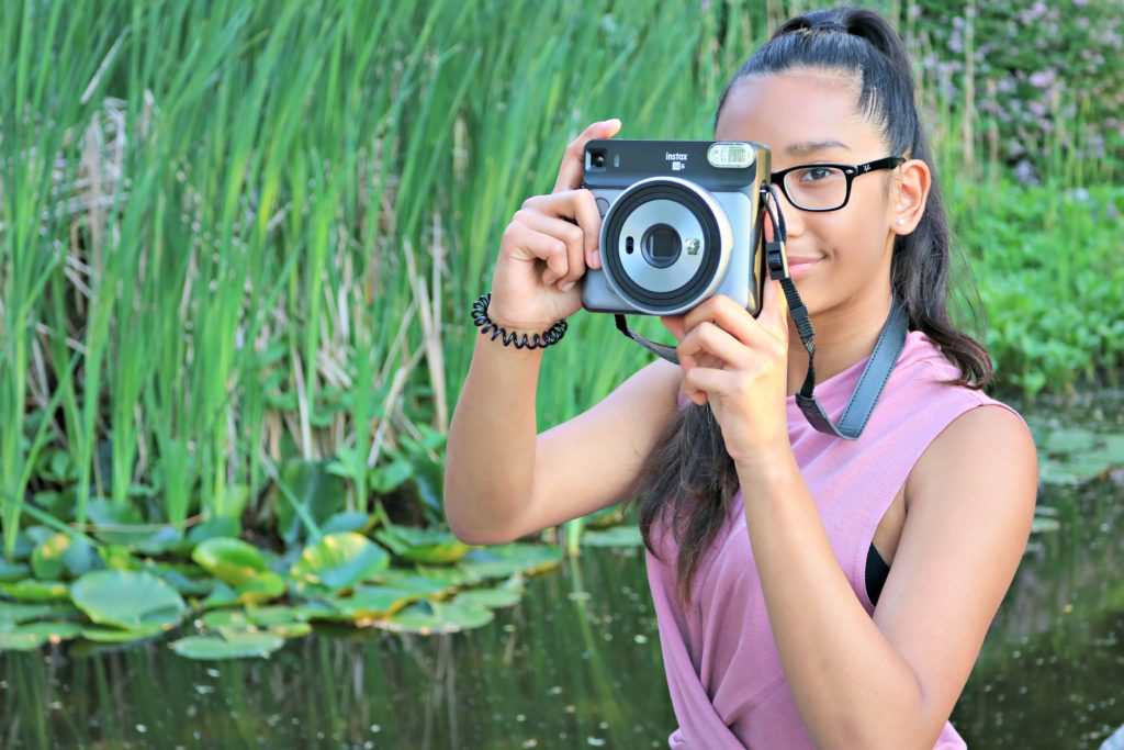 A girl looks into the camera while holding the Instax Square.