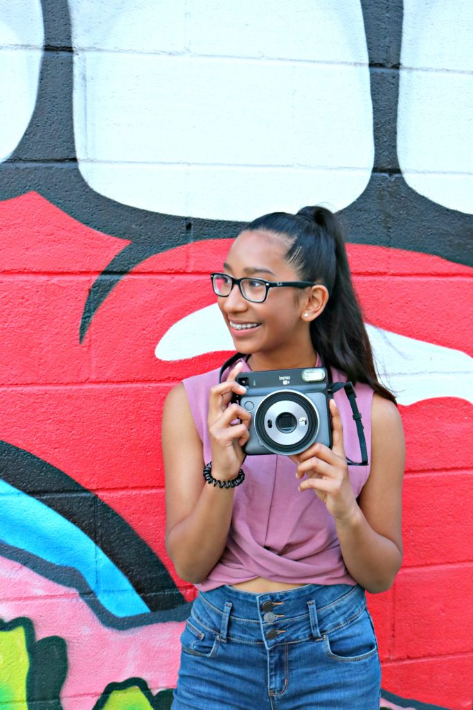 A girl smiles and poses in front of a graffiti wall. 