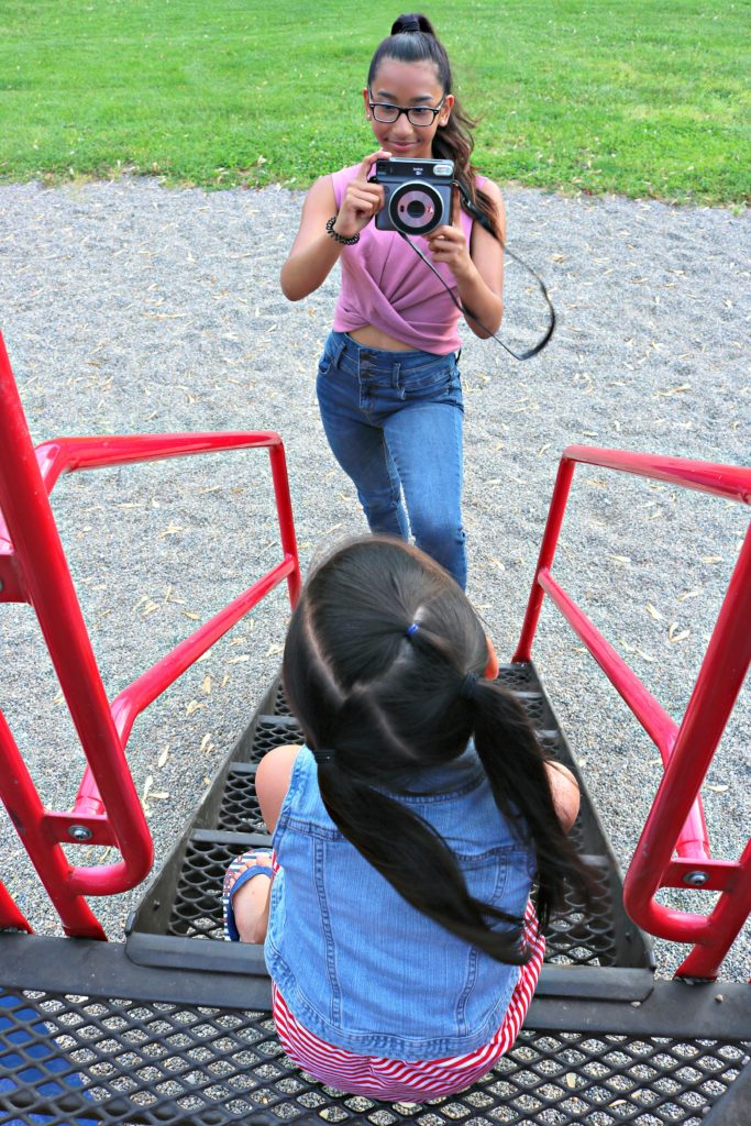 A teen girl takes a picture of her younger sister at the playground. 