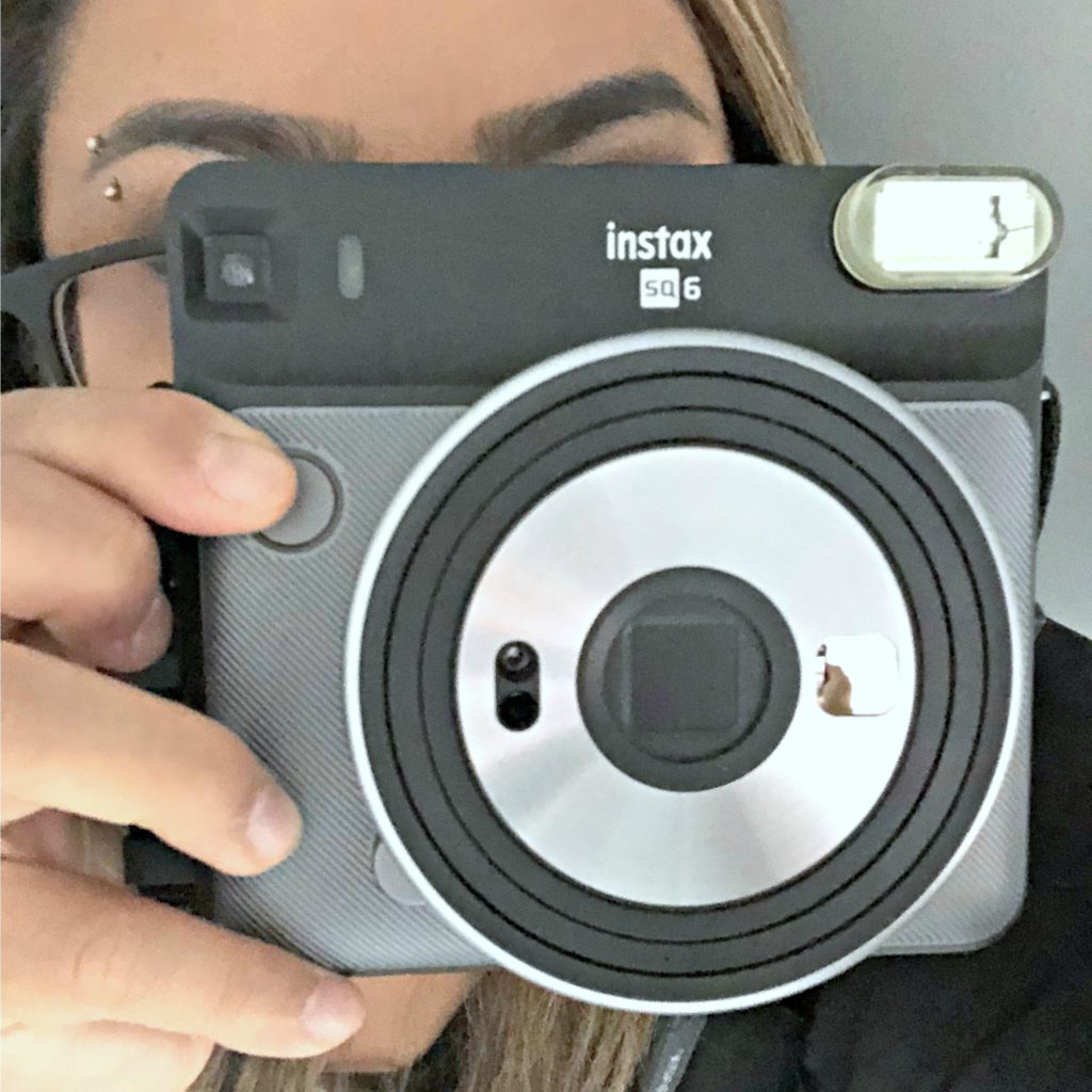 A woman closes in on the camera by pointing an instant camera.