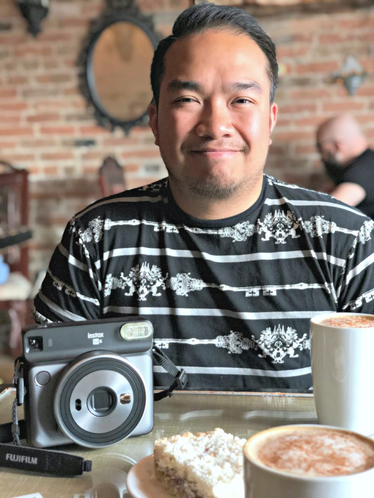 A man smiles at the camera while he enjoys his time in a cafe.
