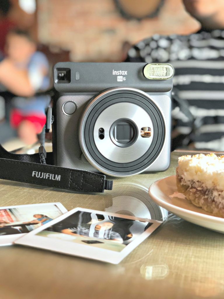 The Instax camera sits on the table while a man enjoy a latte.