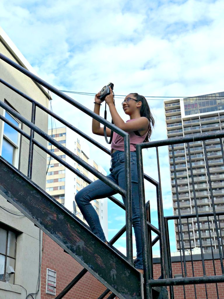 A girl goes up a fire escape to take a snap of a graffiti wall. 