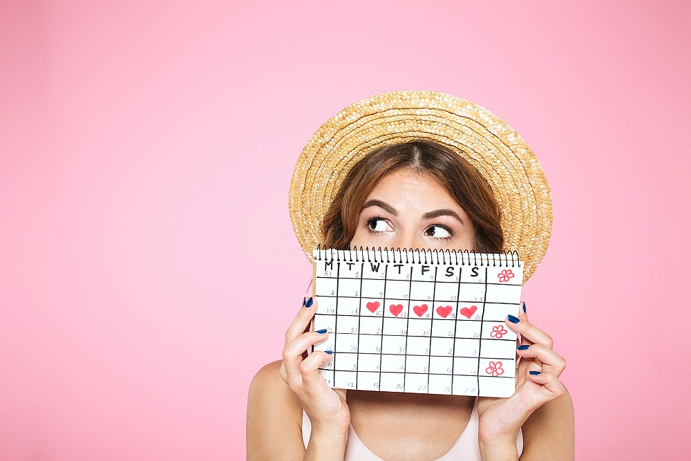 Woman holds her menstrual cycle on a calendar in front of her face.