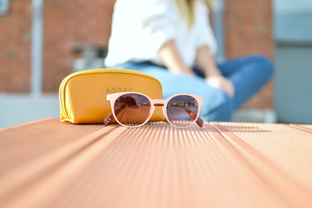 Woman sits in the background on a bench while a pair of sunglasses is the main focus. 