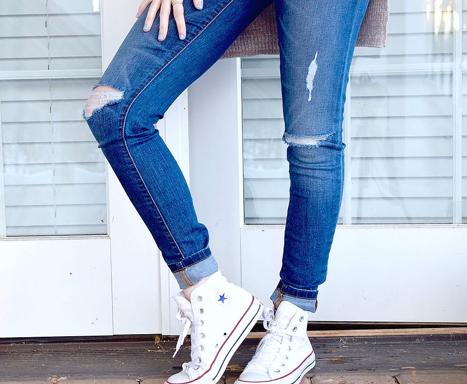 A woman stands in front of the door, only her lower half is visible, she is wearing sneakers. 