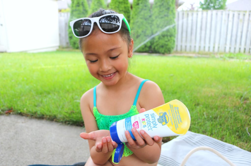 A little girl puts on sunscreen before playing in the sprinkler. 