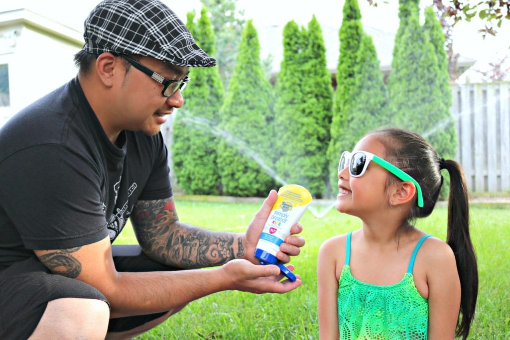 A little girl looks at her dad while applying Banana Boat Lotion sunscreen. 