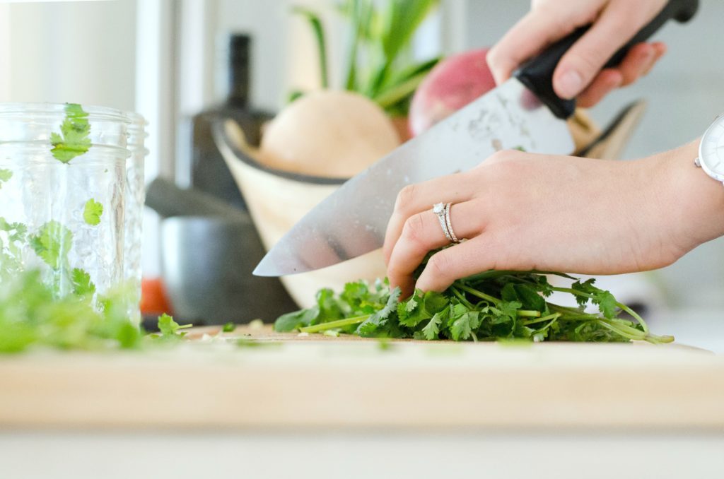 A woman cooks at home and chops parsley.