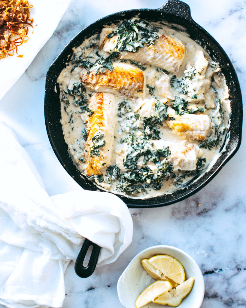 A cast iron with fish, cream, and spinach. A dish that shows how good fish is and the healthy benefits of eating fish.