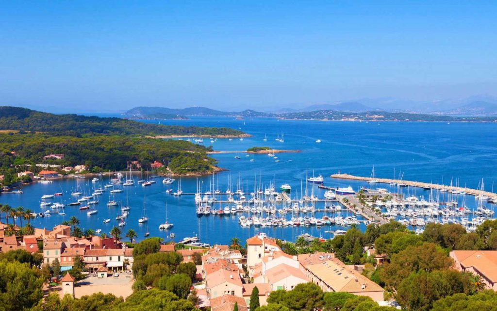 The island of Porquerolles is lined with sail boats and navy blue water. 