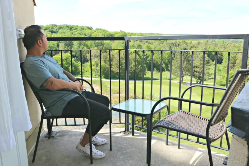 A man sits in a chair on the balcony of his Executive Suite.