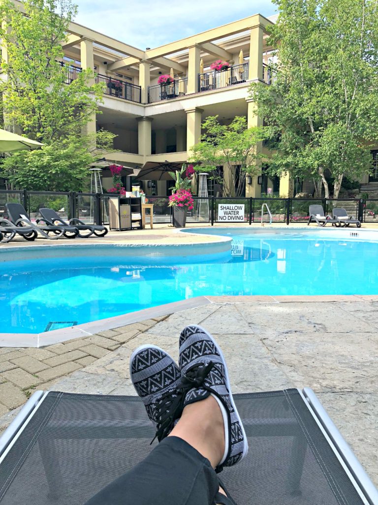 A woman sits in a patio chaise with her legs crossed, feet are visible, outlooking the gorgeous Hockley Valley Resort pool. 