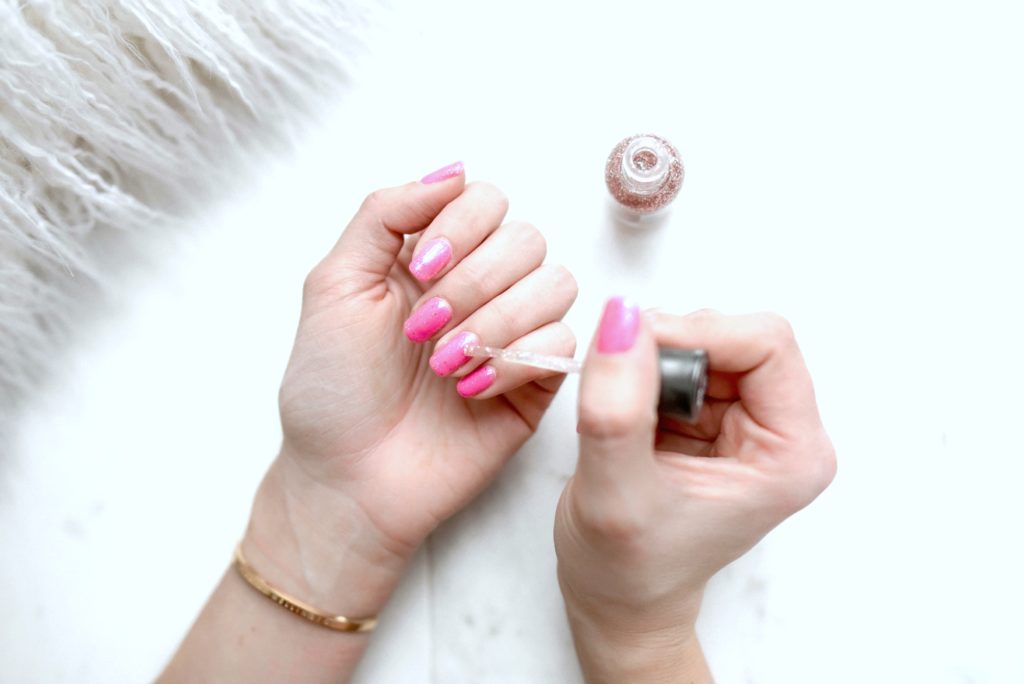 A woman does her nails and puts glitter polish on top of a pink nail polish. 