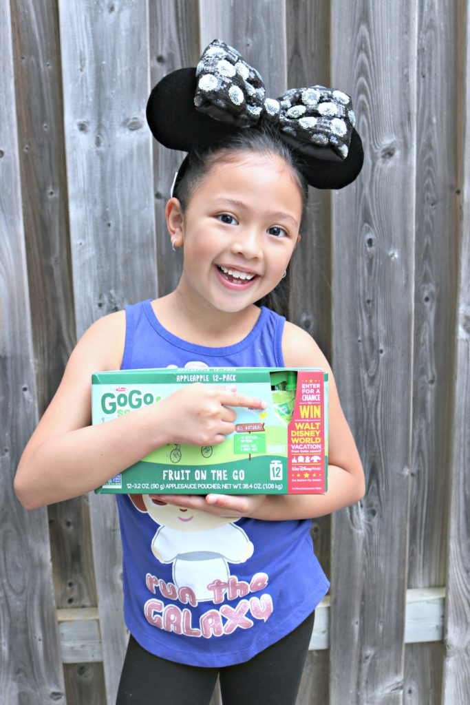A little girl wears a GoGo SqueeZ box and points to instructions to win a trip to Disney World.
