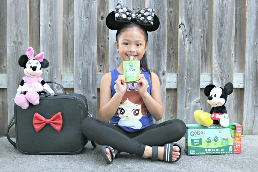 A little girl enjoys a GoGo SqueeZ with Mickey and Minnie with a box of GoGo SqueeZ with instructions on how to win a trip to Disney World. 