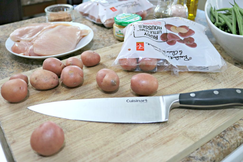 A knife is shown on a cutting board with red potatoes and other ingredients.