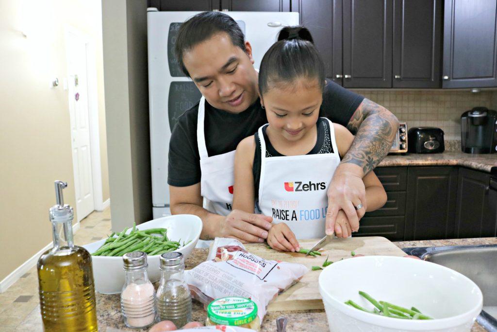 A little girl and her dad chop vegetables together. 