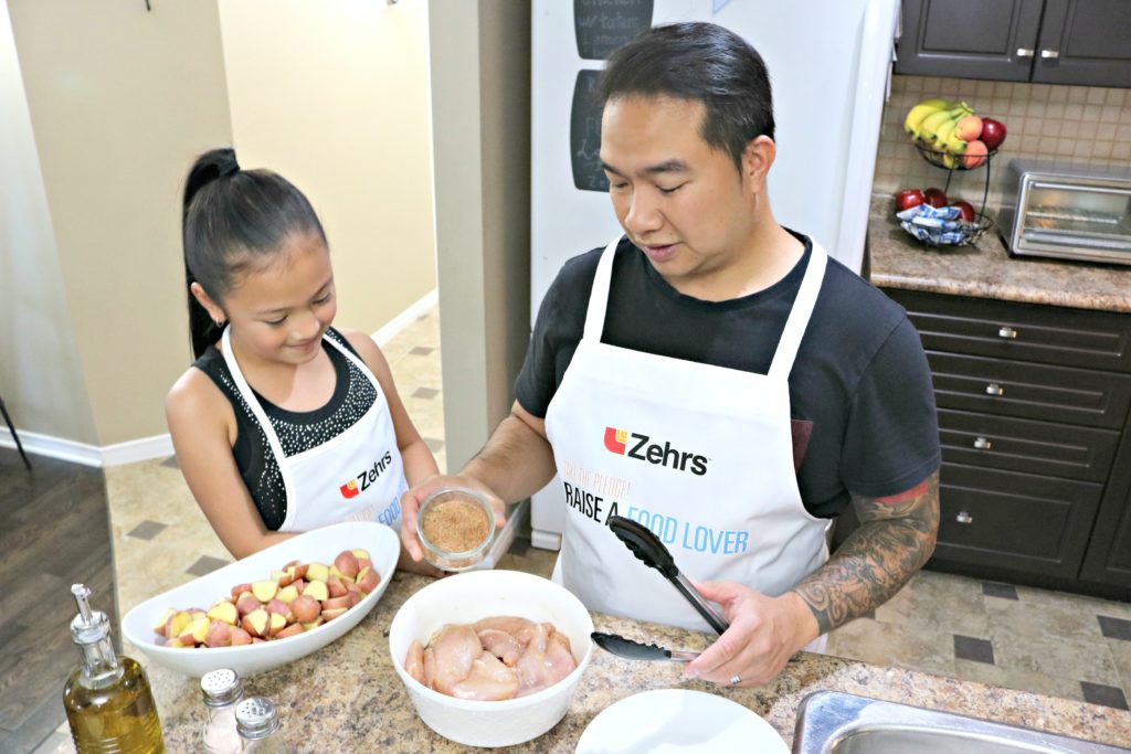 A dad adds house blend of spices over chicken breasts.