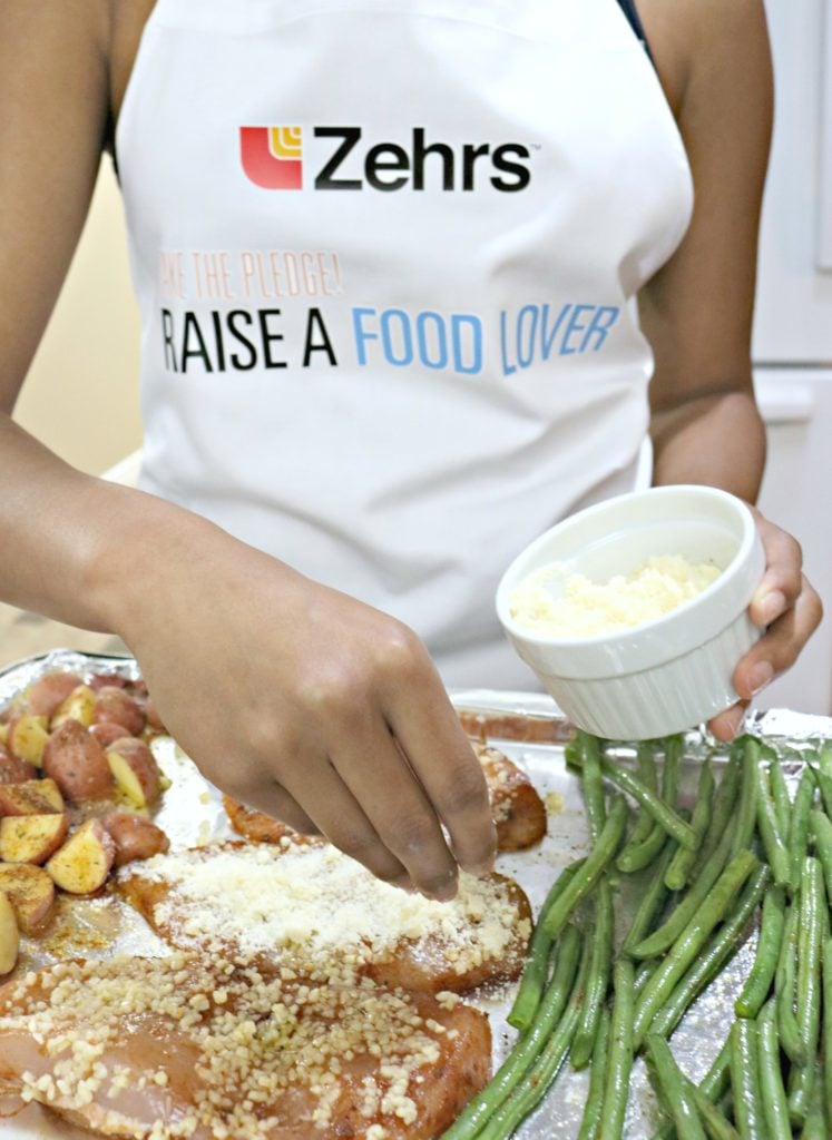 A girl adds parmesan to the one-pan Parmesan garlic chicken dinner.