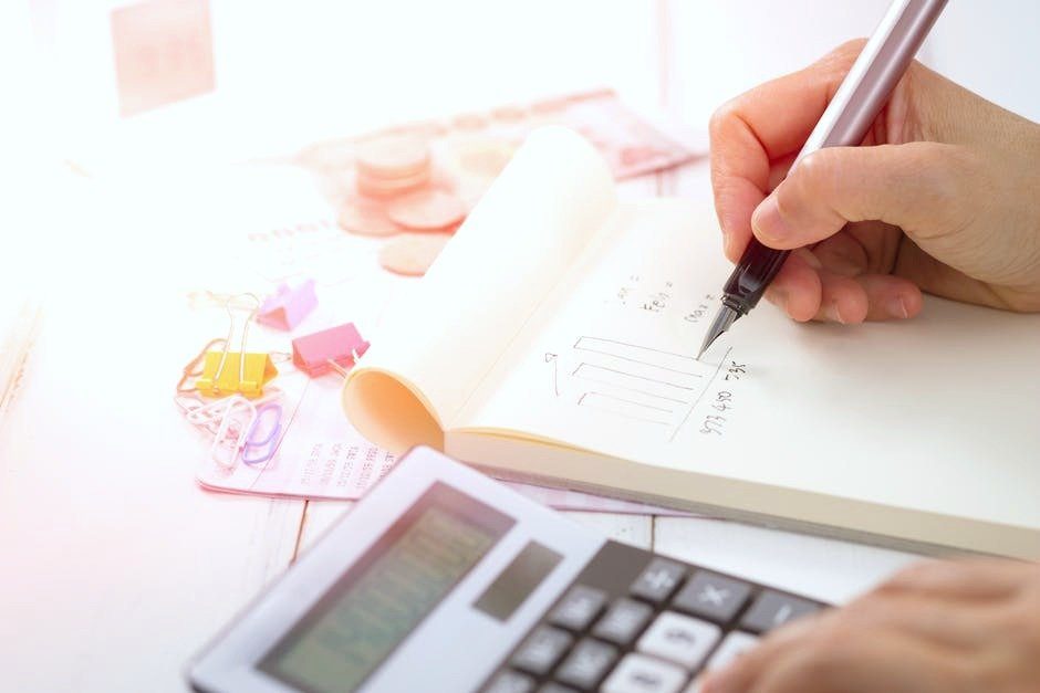 A person writes down a budget and a note pad, pen, and calculator is shown. They are writing down financial tips that help you save more.