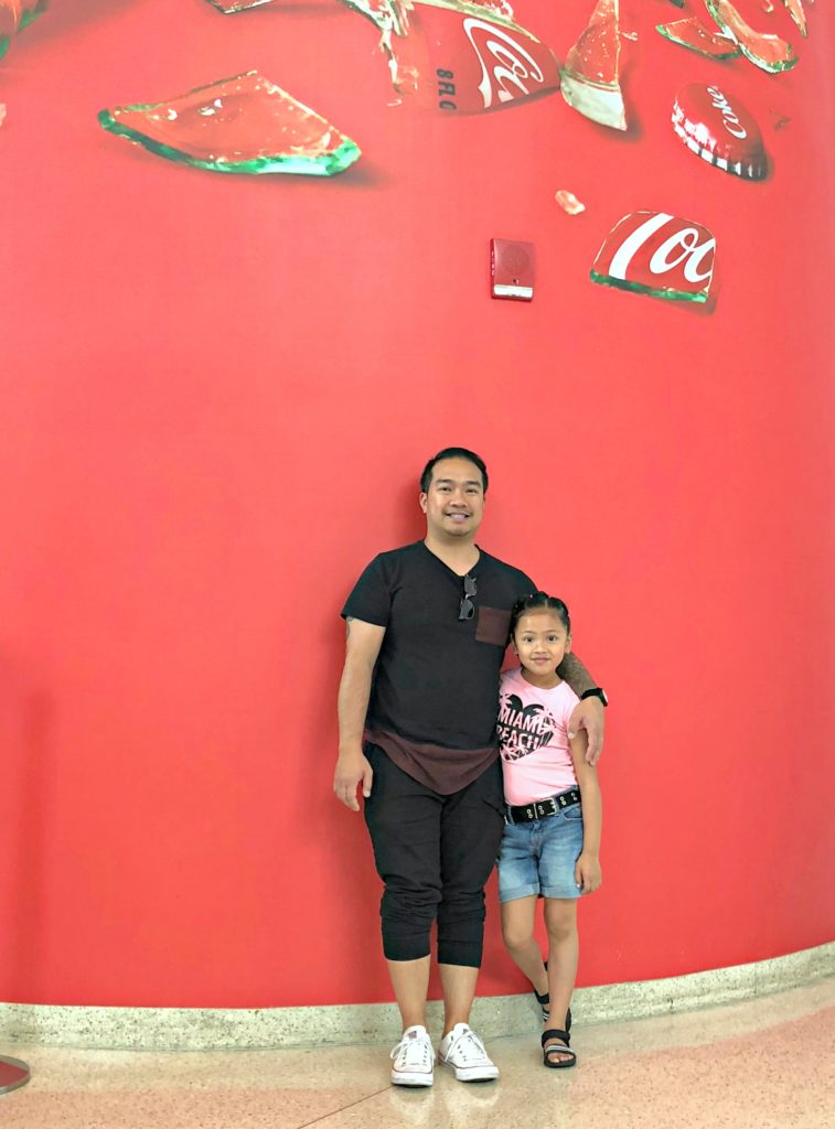 Little girl and her dad stand inside the World of Coca-Cola.