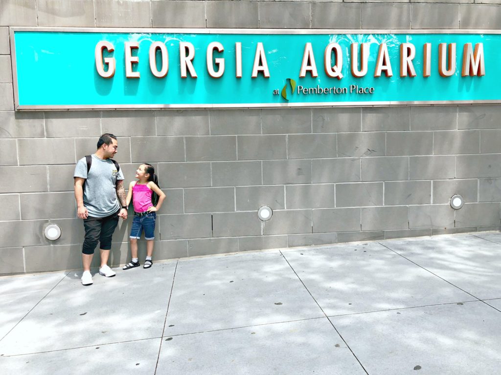 A girl and her father stand in front of the Georgia Aquarium sign.