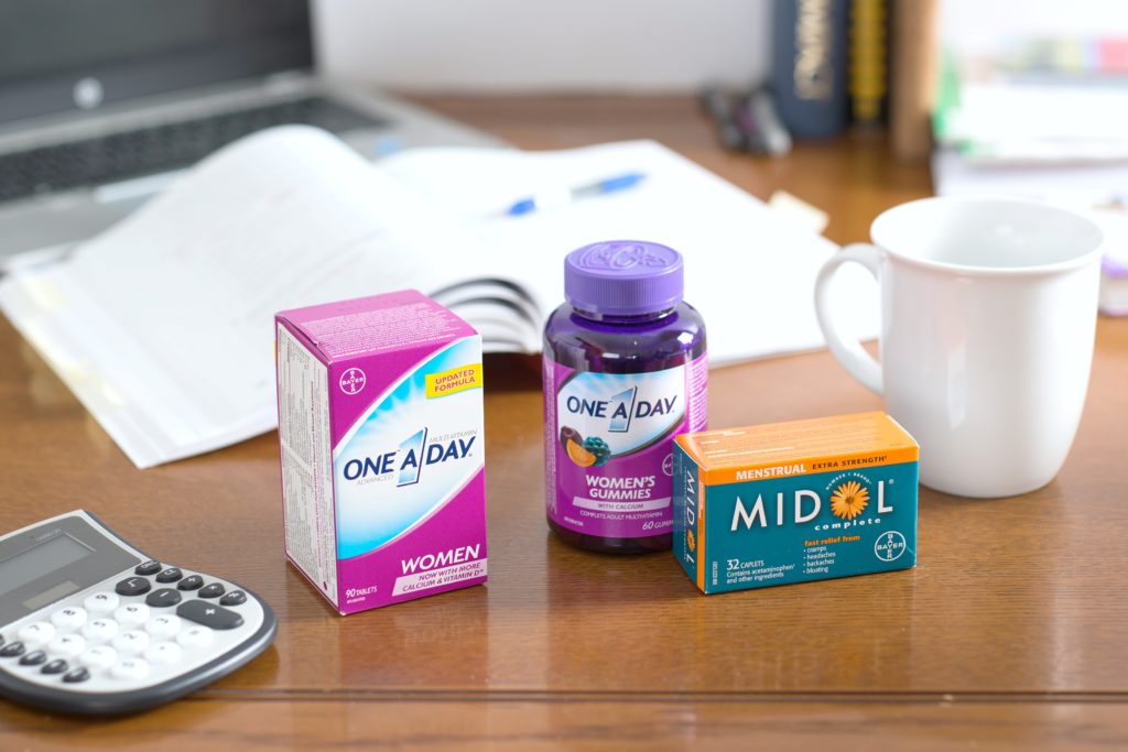 A computer desk is shown with One a Day vitamins and Midol. 