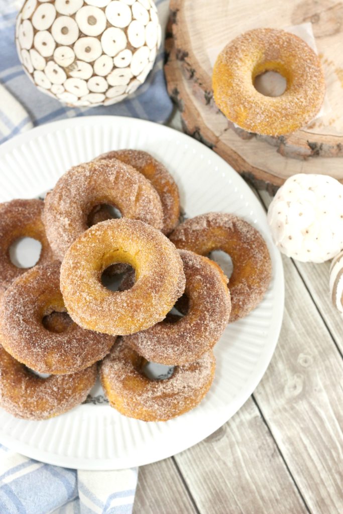 A plate is fully stacked with sugar coated baked pumpkin spice donuts, surrounded by fall decor.