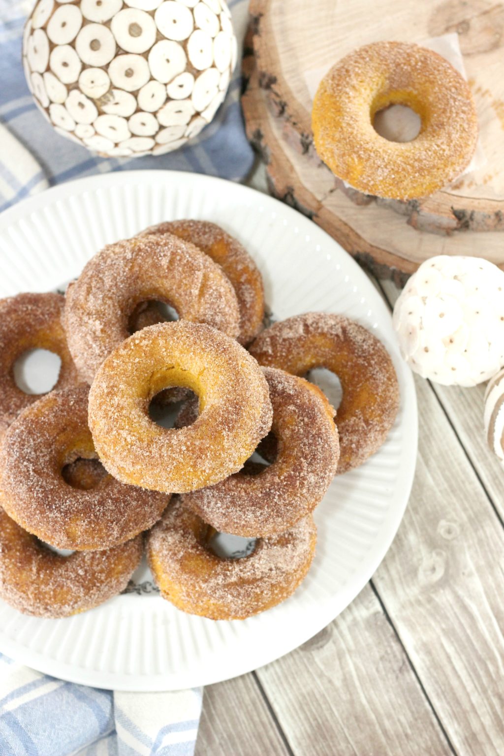 Fall is in the air and you if are anything like me, fall time is pumpkin spice everything time. Try these easy delicious baked pumpkin spice donuts! #recipes #pumpkinspice #donuts A plate is fully stacked with sugar coated baked pumpkin spice donuts, surrounded by fall decor.