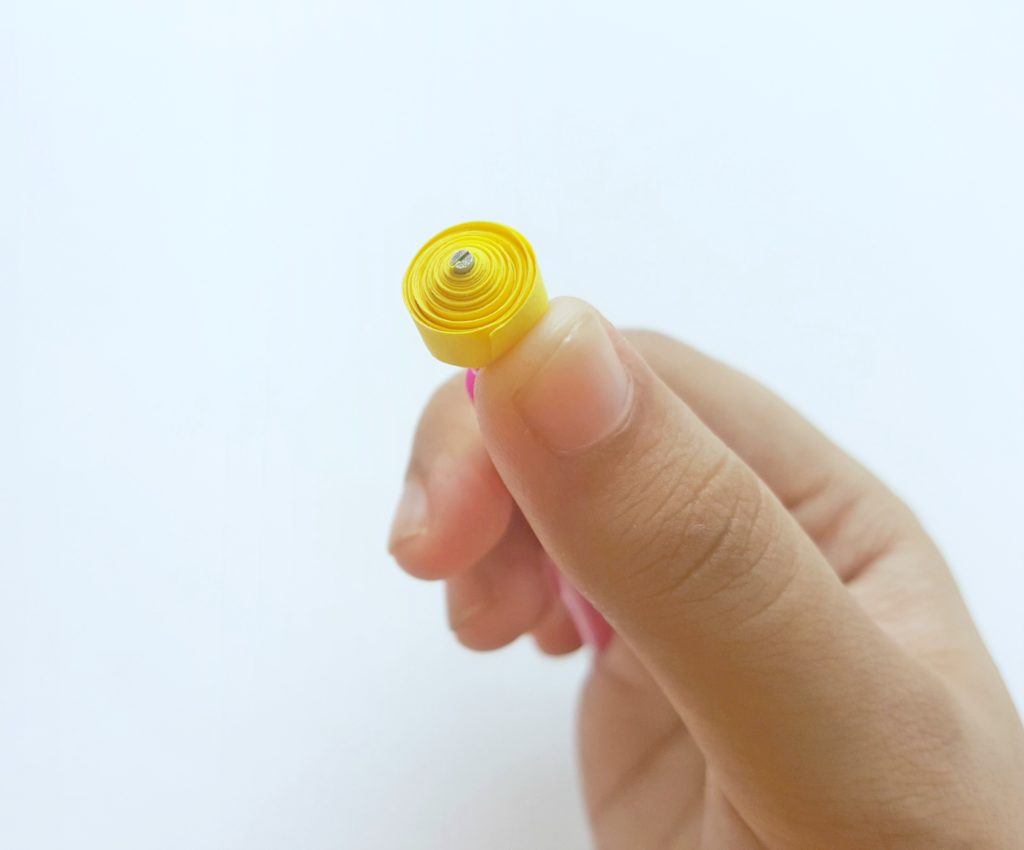 A piece of yellow paper is tightly coiled around a quilling tool. 