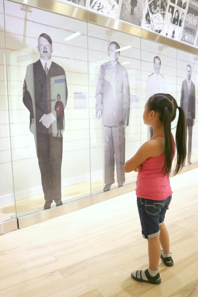 A little girls stands with her arms crossed while she learns about the world's most notorious dictators.