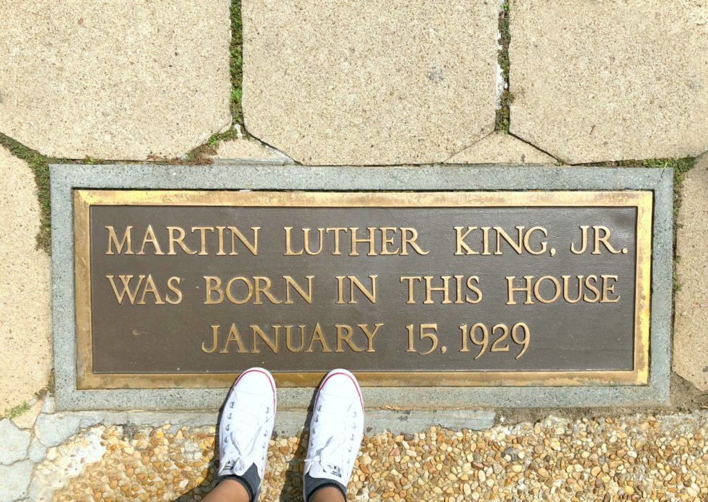 Feet are shown standing in front of MLK's childhood home and plaque naming it so.