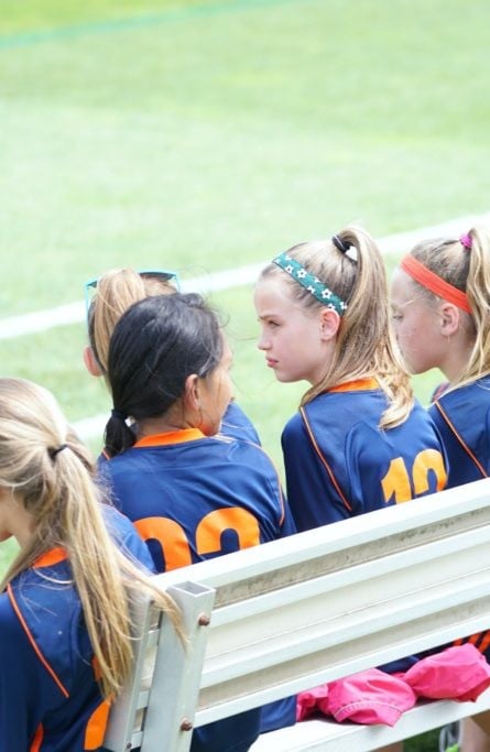 Girls on the bench during soccer game. This article shares tips for protecting kids who play sports.