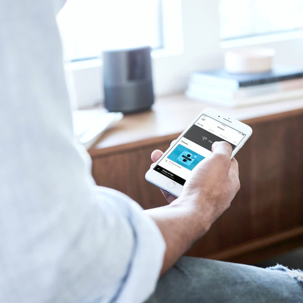 Man sits while holding an iPhone and listening to Ed Sheeran connected to a Bose speaker.