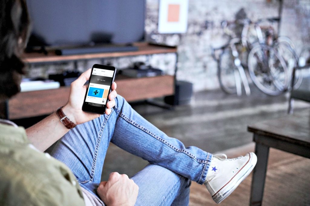 Man holds his cell phone while connecting to Bose speakers and soundbar.