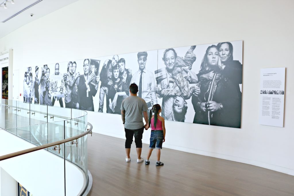 A father and his daughter hold hands while looking at a mural on the wall at the Center for Civil and Human Rights. 