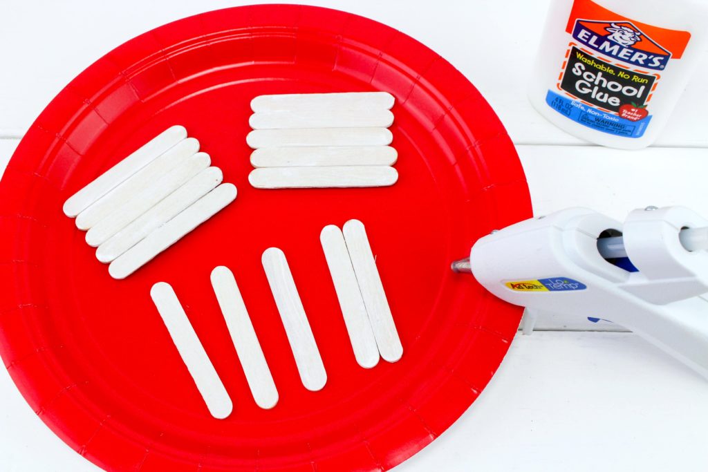 Red plate with mini popsicle sticks being glued together. 