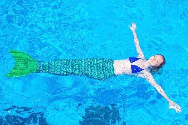 A woman dressed as a mermaid is shown swimming in a pool. 