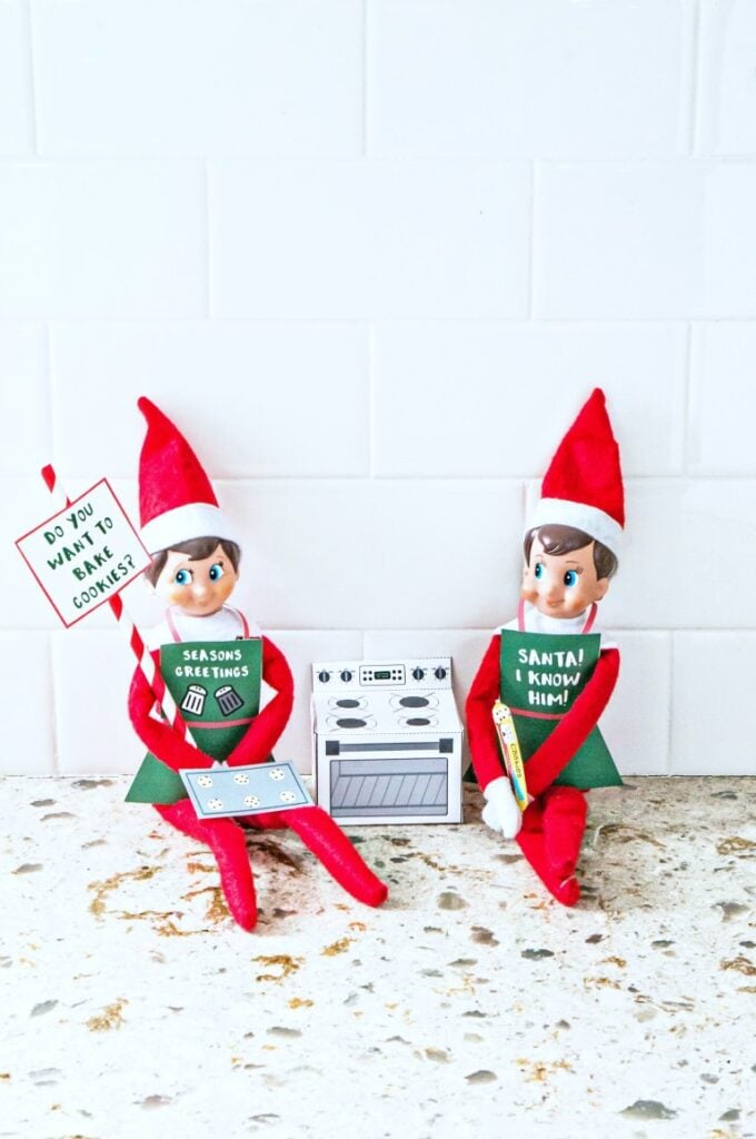 Two elves on the shelf posing with signs and an oven.