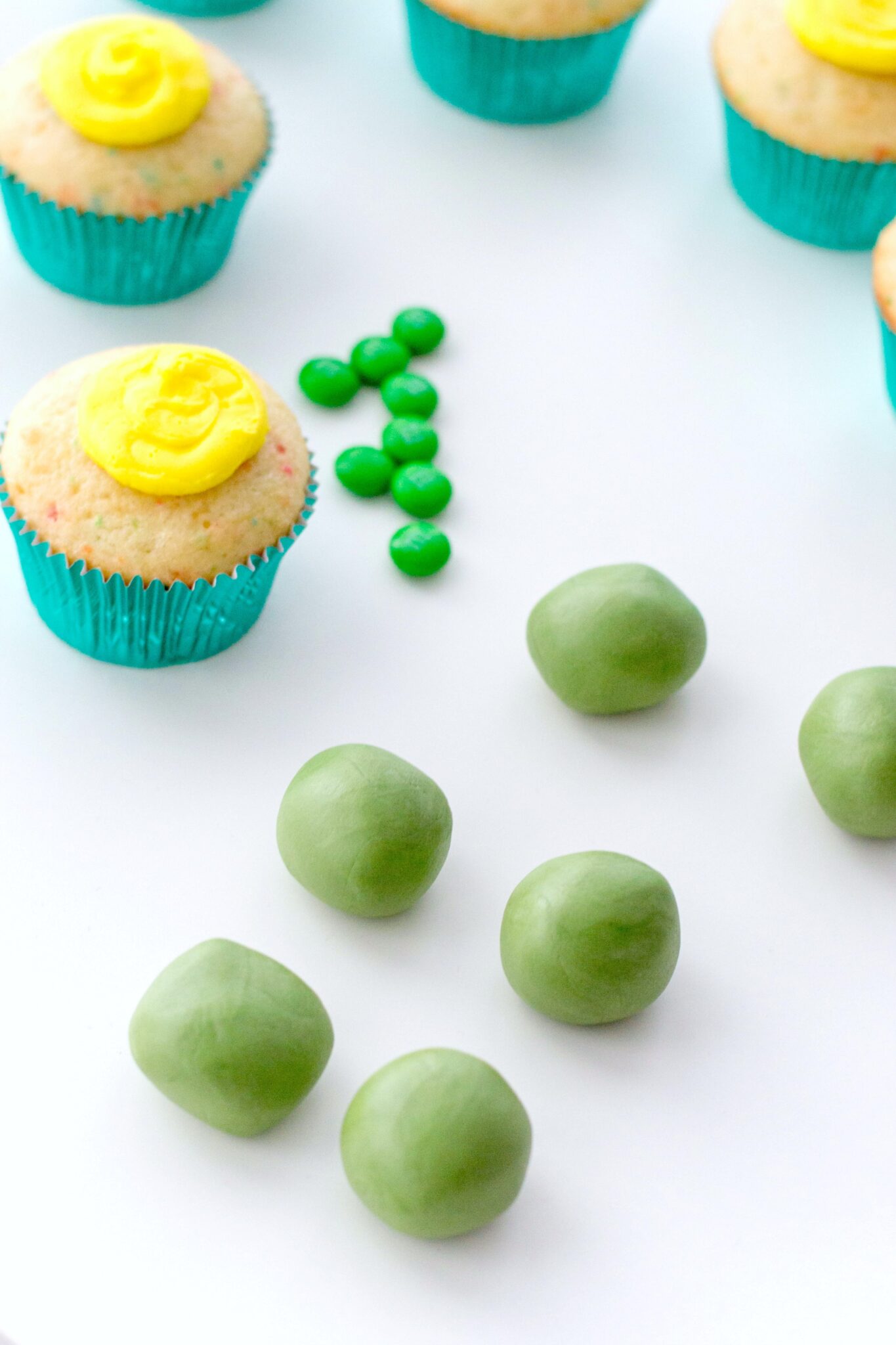 Green fondant rolled into balls alongside iced funfetti cupcakes. 