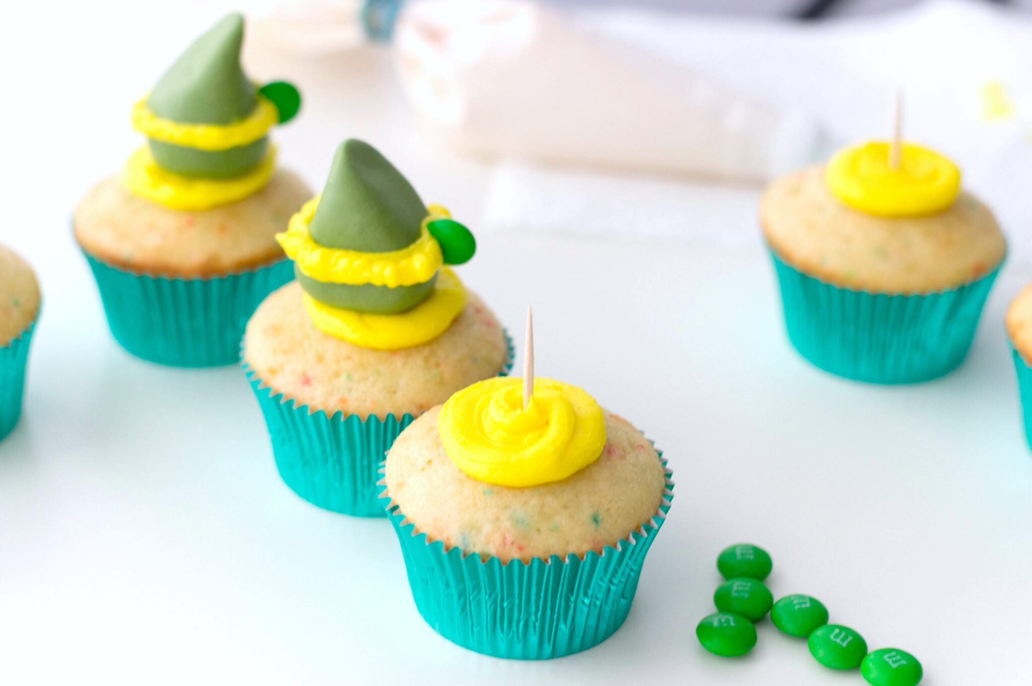Funfetti cupcakes with a toothpick placed in the middle of buttercream to hold fondant elf hat. 