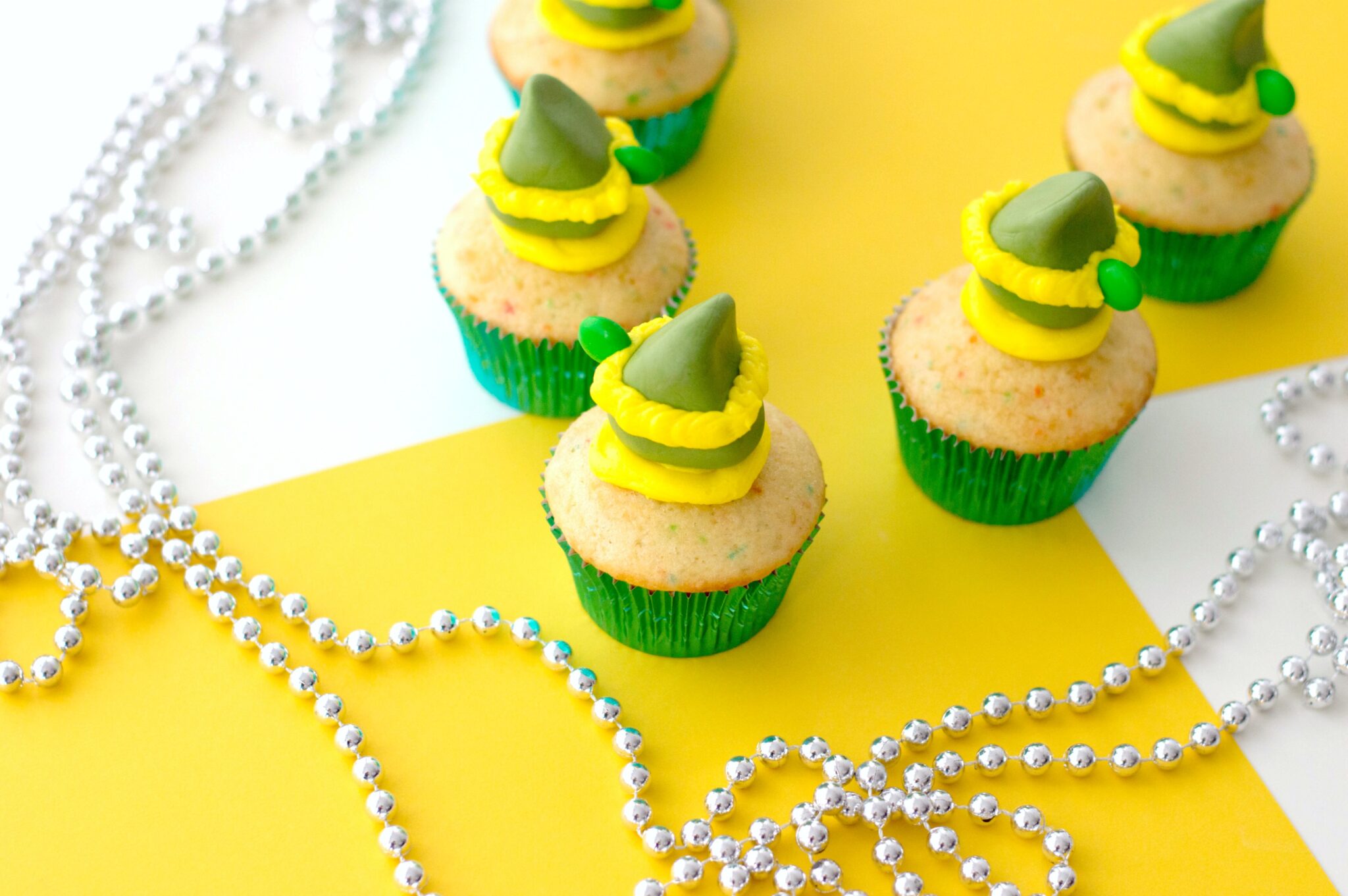 Final product with 5 Buddy the Elf cupcakes shown against a yellow and white background and silver bead garland. 