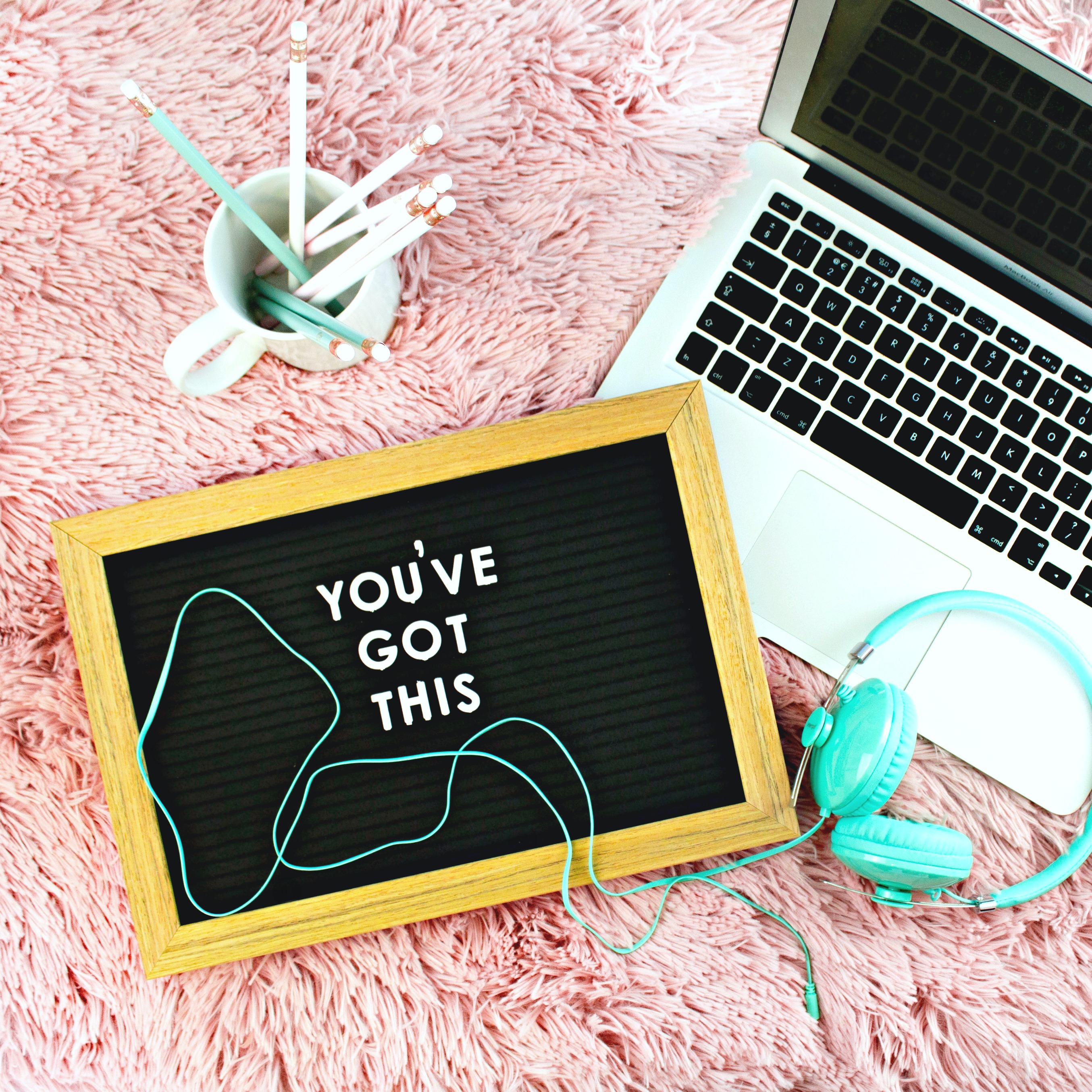 An inspirational sign, pencils in a cup, headphones and a laptop for job searching are shown. 