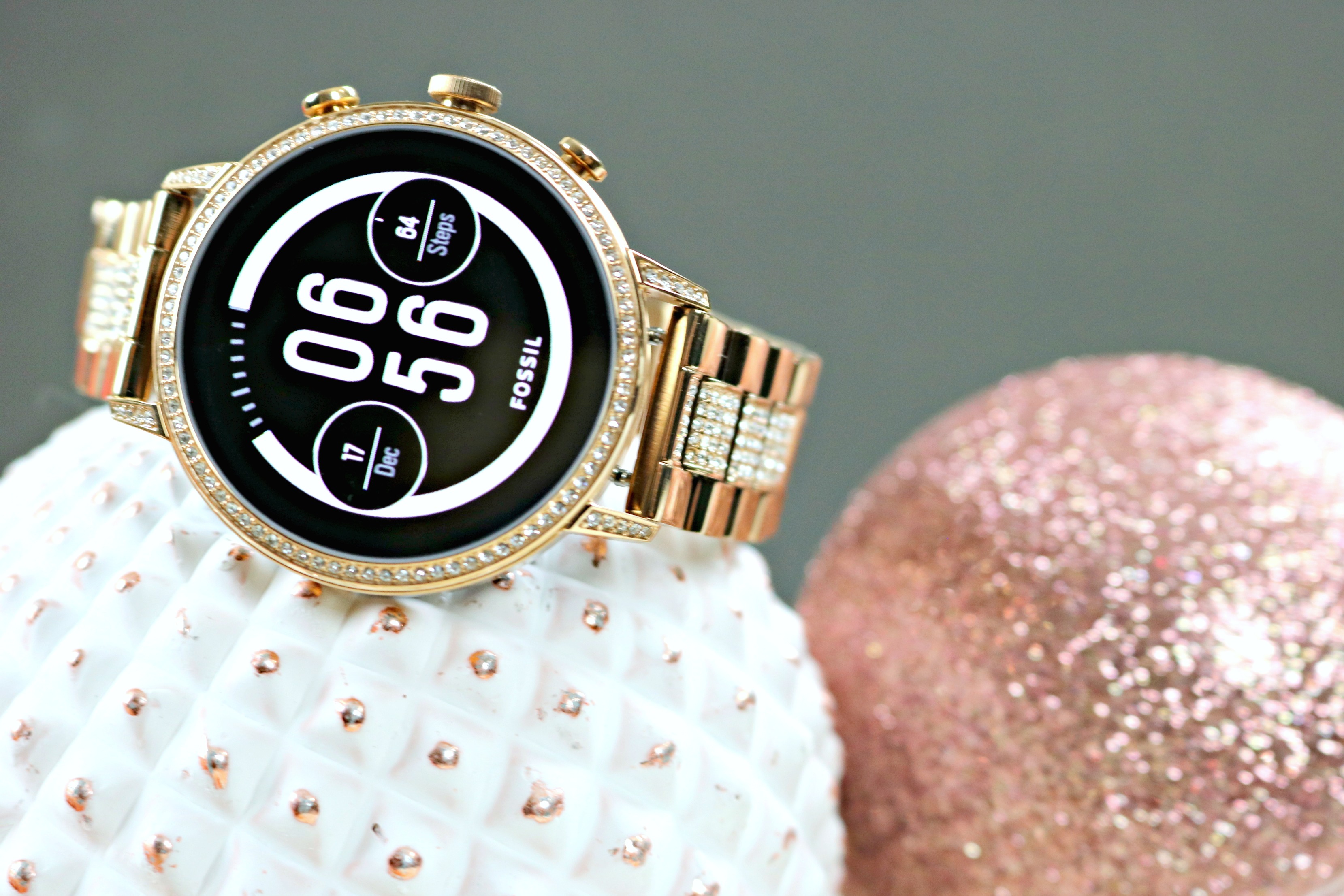 Fossil Smartwatch sitting on top of rose gold ornaments. 