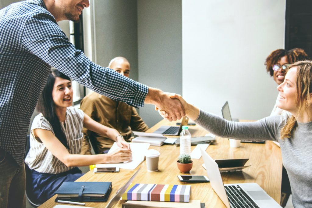 A woman shakes her interviewers hand while other interviewers who look on and smile. 