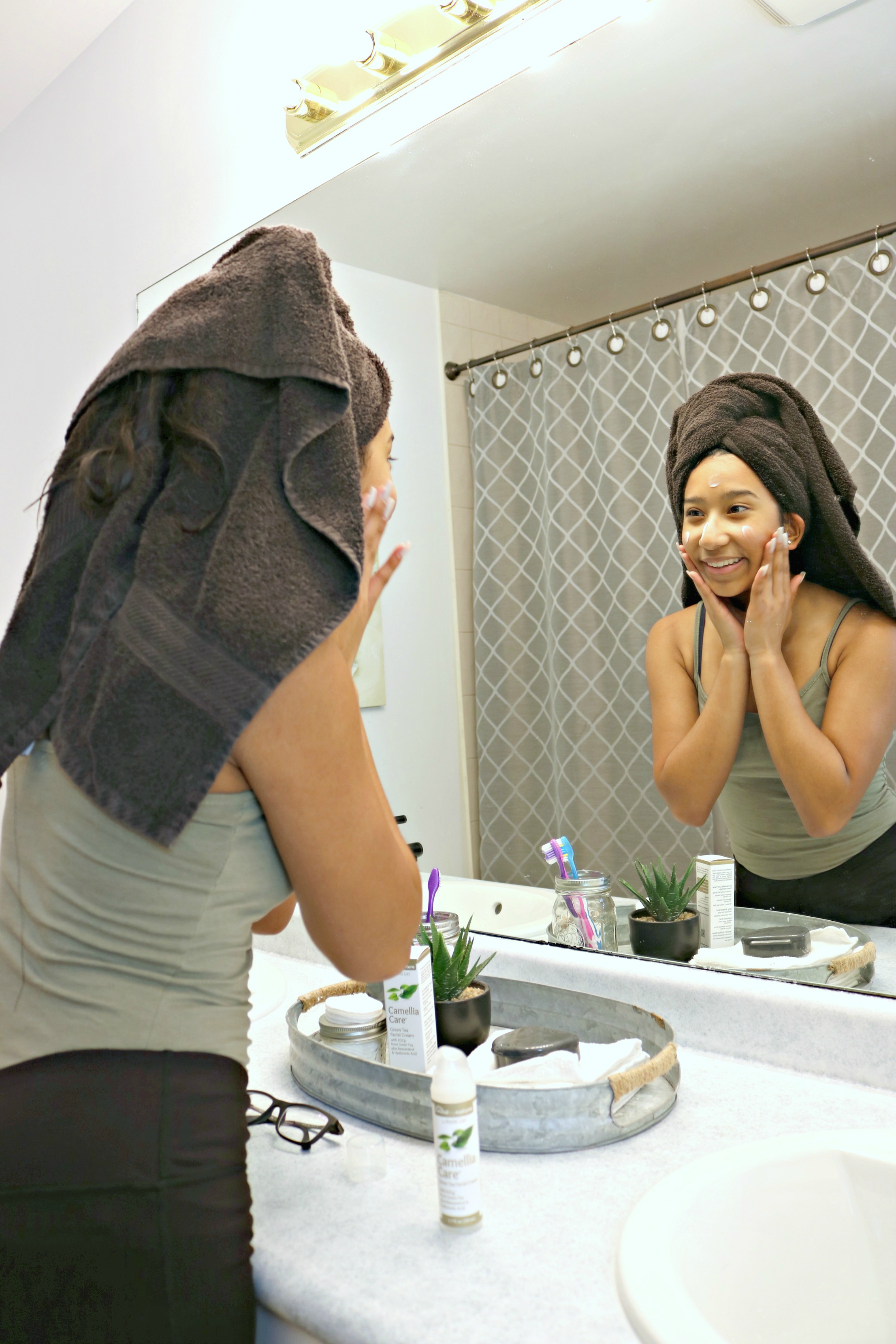 Young woman puts on moisturizers and smiles into mirror. 