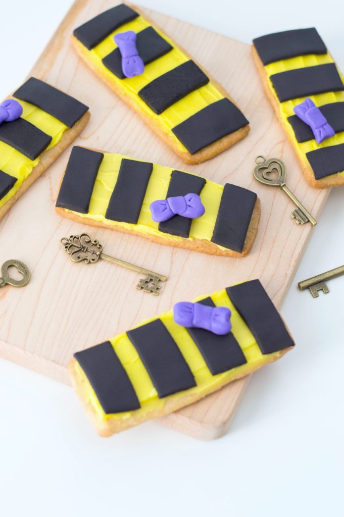 The final product of Hufflepuff Scarf Sugar Cookies on a wooden board, with whimsical skeleton keys surrounding them for decoration.