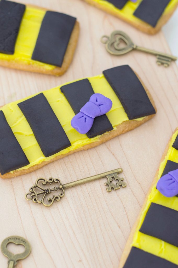 Hufflepuff Scarf Sugar Cookies are shown close up against a wooden board with whimsical keys surrounding them for decor purposes only. 