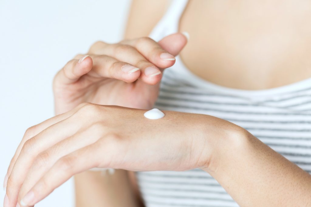 Woman applies lotion/sunscreen, only her hands are visible.